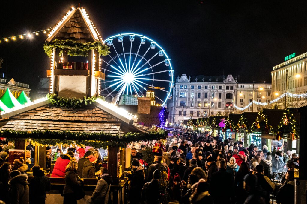 Crowded night market with neon lights and ferris wheel creating a festive atmosphere. Low Budget Travel Hagenberg