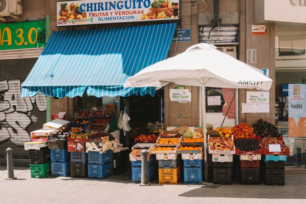 Vibrant outdoor produce store in Valencia displaying fresh fruits under a blue awning. Low Budget Travel Hagenberg