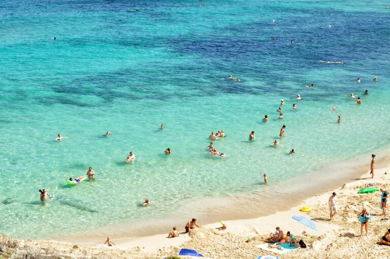 People enjoying a sunny day at a beautiful beach in Hagenberg, with turquoise water and sandy shores. Billigreisen Hagenberg